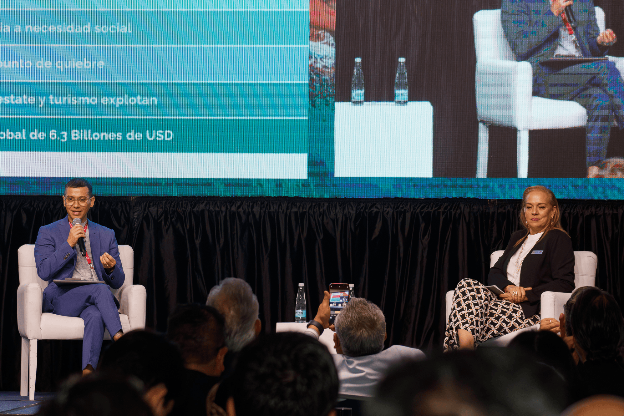 Fran Lugo, especialista en turismo wellness, participa como ponente en el Congreso AMDETUR 2025, sentado en el escenario junto a Ana Acevedo, frente a una audiencia, con una pantalla gigante mostrando parte de su presentación.